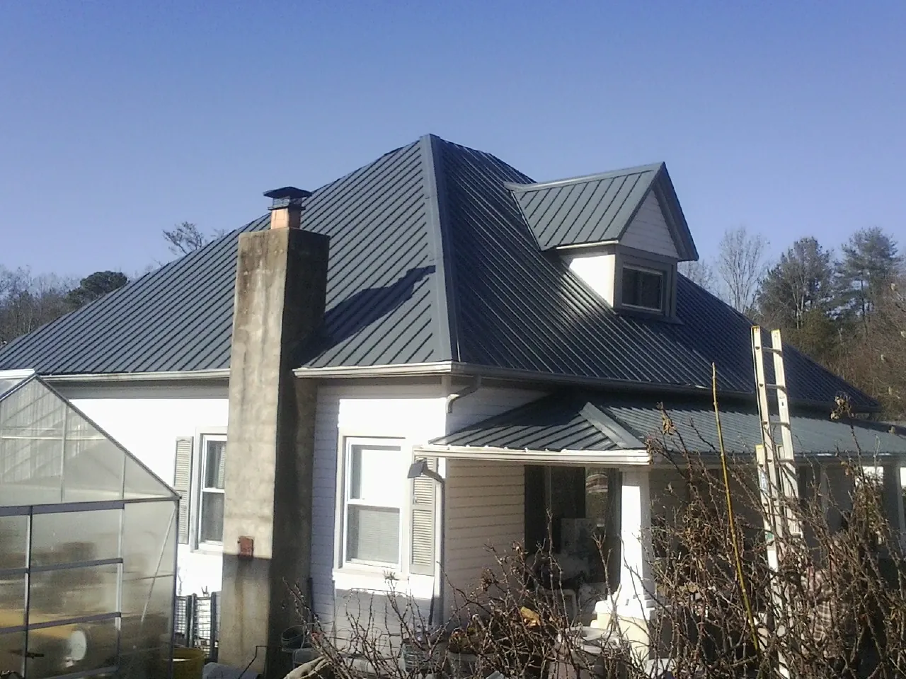 Dark blue standing seam metal roof on a white farmhouse with dormer — Slate & Tile Roof Repair by Roofing Brothers in Columbia Falls