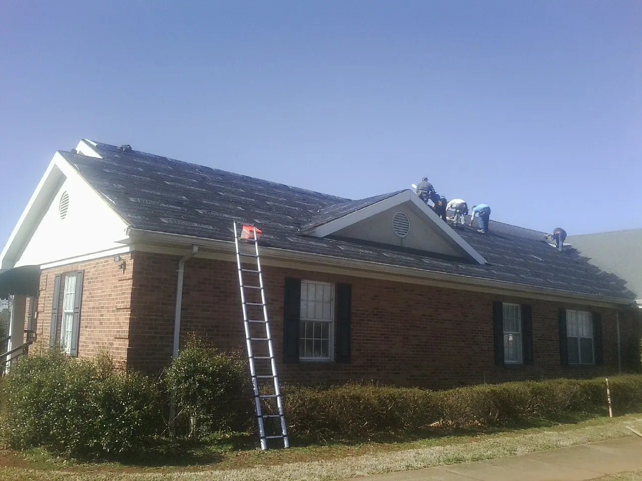 Crew tearing shingles off a brick ranch roof with a ladder set — Emergency Roof Repair work by our crew in Columbia Falls