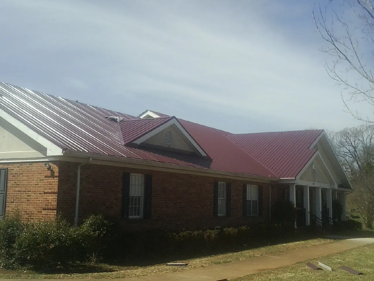 Red metal roof with gabled entries on a long brick building, from a Hail Damage Roof Repair job in Columbia Falls