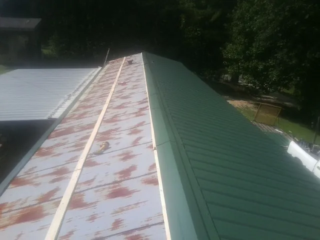 Old rusted panels beside newly installed green metal roofing — Wind Damage Roof Repair by Roofing Brothers in Columbia Falls