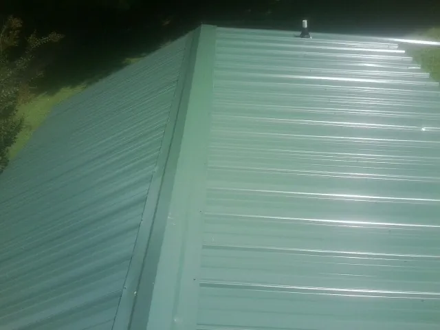 New green metal panels meeting at the ridge of a roof — Flat Roof Repair work by our crew in Columbia Falls