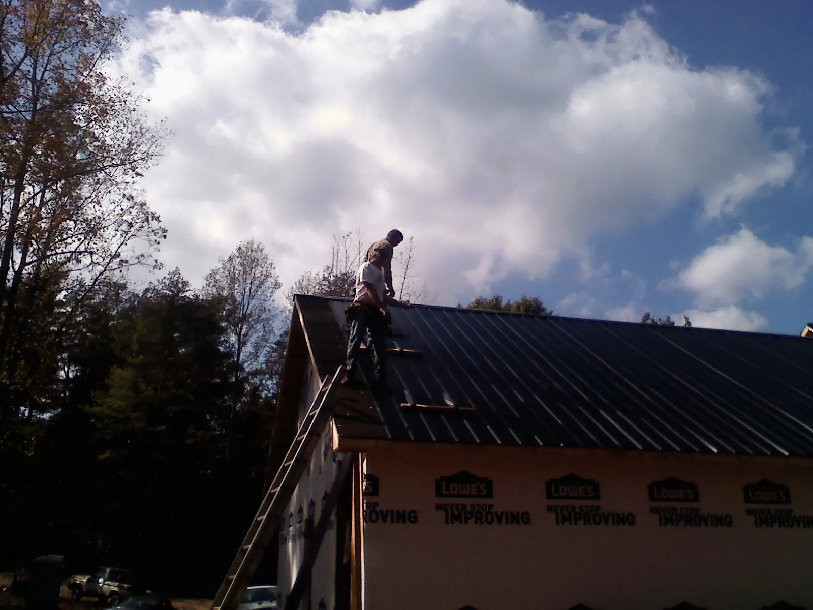 Roofer fastening dark metal panels high against a cloudy sky, from a Roof Inspection job in Columbia Falls