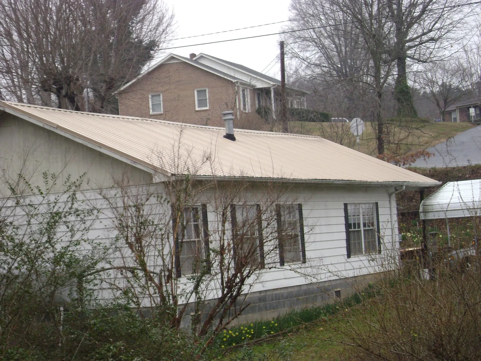 Tan metal roof on a white sided house set into a hillside — Commercial Roofing by Roofing Brothers in Columbia Falls
