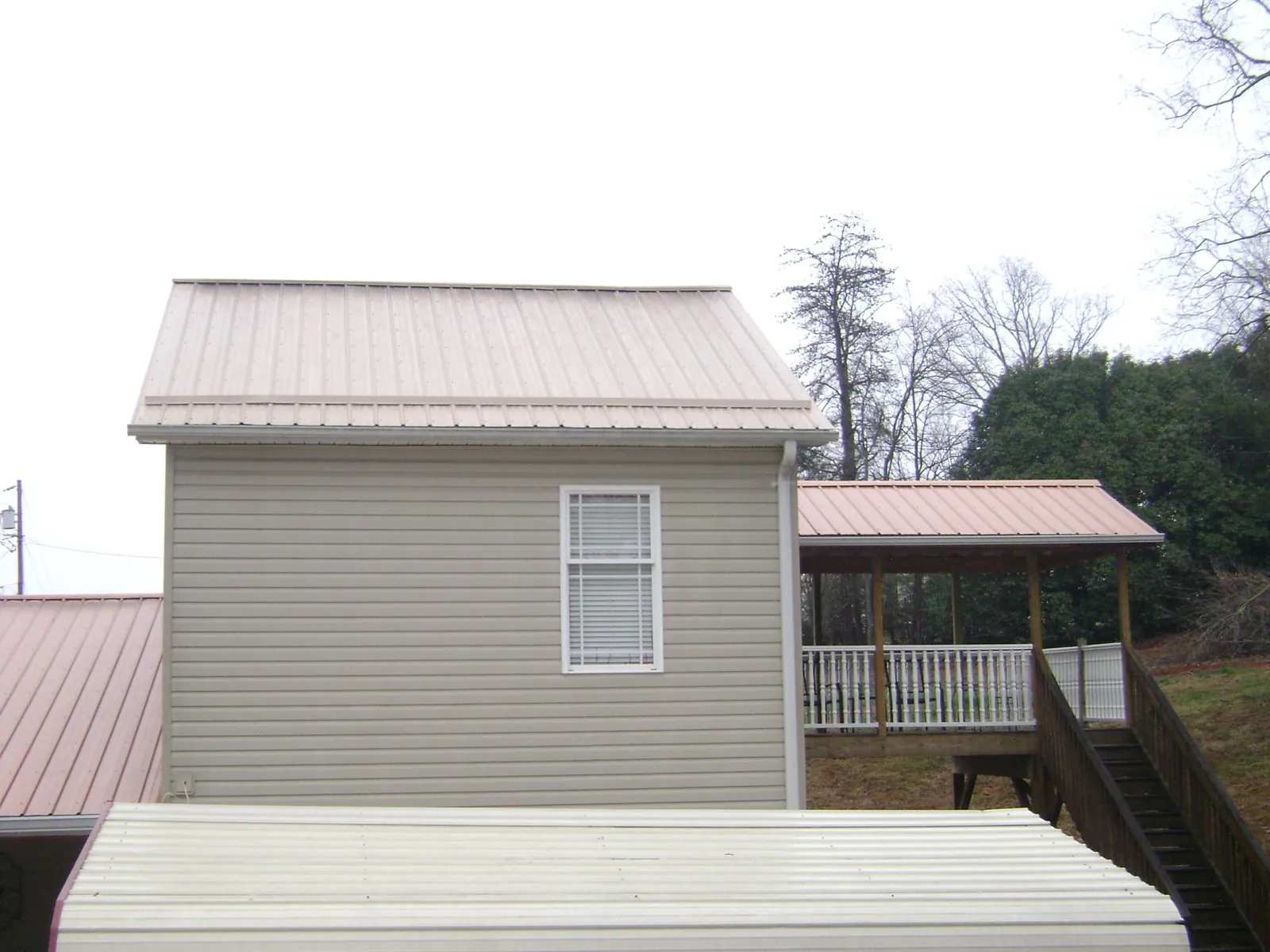 Tan metal roofs on a two story addition and attached porch, from a Roof Replacement job in Columbia Falls