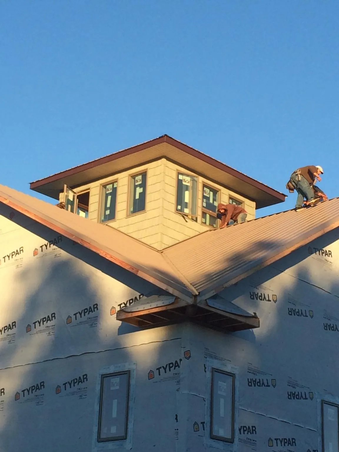 Roofers working around a rooftop cupola on a new metal roof at sunset — Roof Waterproofing in Columbia Falls by Roofing Brothers